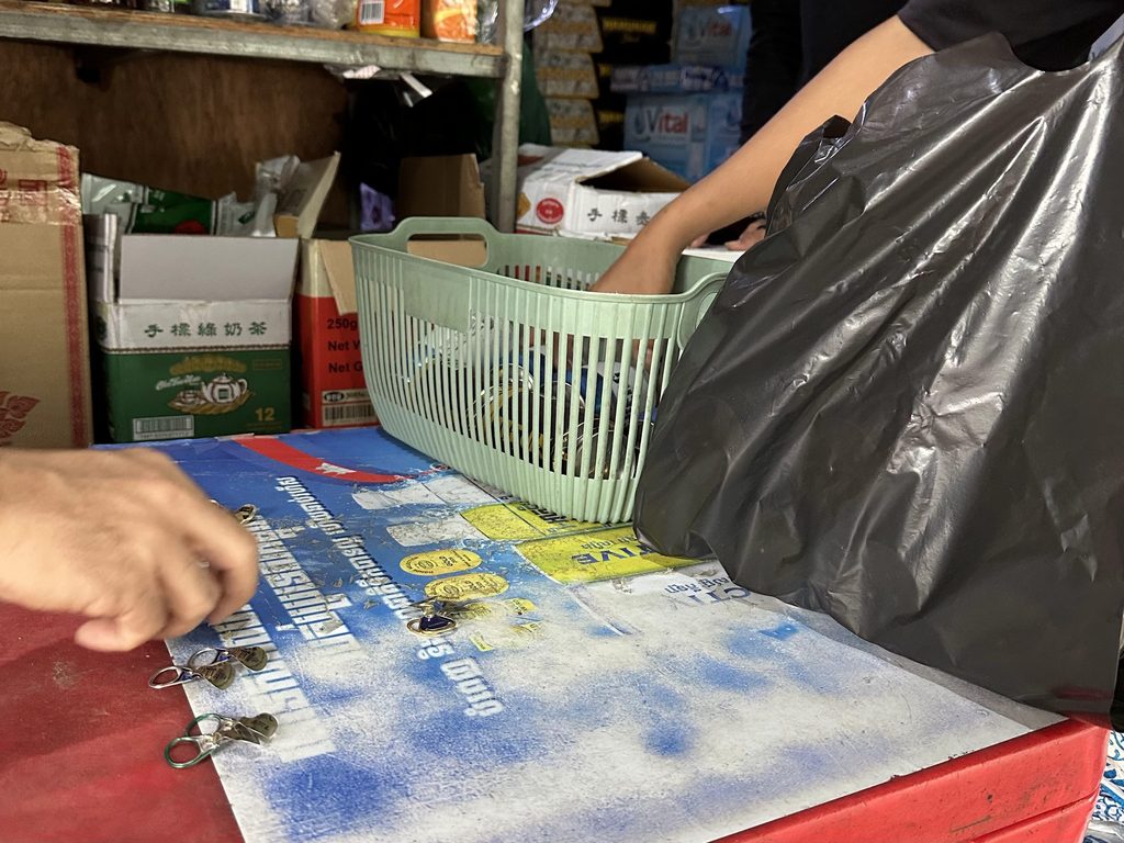 プノンペンのローカル商店のカウンターで、店主が当たりくじのプルタブを数え、黒い袋に缶ビールを詰めているようす